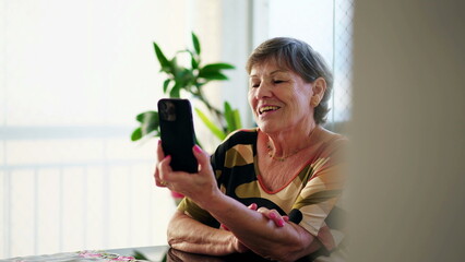Candid Senior Woman waving hello and Holding Phone while Engaging in Video Communication feeling...