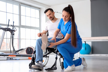 Female physiotherapist working with young man in wheelchair at rehabilitation center