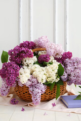Wicker basket with beautiful fragrant lilac flowers near white wooden wall