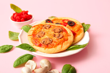 Plate with different tasty mini pizzas and ingredients on pink background