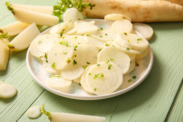 Plate with slices of fresh daikon radish on green wooden background