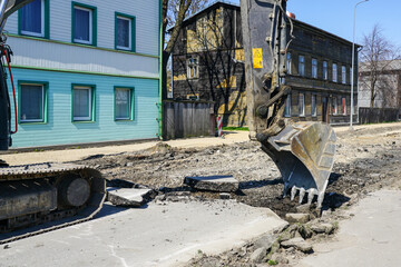 Fototapeta premium Crawler excavator with a bucket dismantle the asphalt before the reconstruction of the street