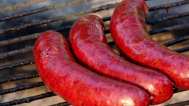 Close up of overcooked sausage bursting with fat while being grilled on the fire pit.