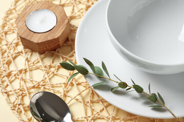 Beautiful table setting with candle and branch on beige background, closeup