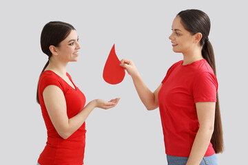Young women with paper blood drop on light background