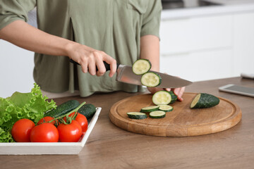 Woman cutting cucumber for salad on wooden table with vegetables