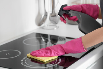 Woman in pink rubber gloves cleaning electric stove with sponge and detergent