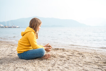 Fototapeta na wymiar Lonely beautiful sad girl teenager sits thoughtfully on sand sea beach. Dreams,anxiety,worries about future,school friends, parents. Teen bullying, psychological problems in adolescent puberty period