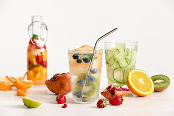 Glasses and bottle of infused water with different sliced fruits on white table