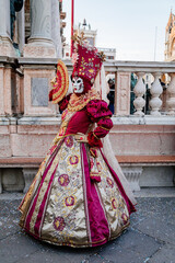 Venice, Italy, 11 February 2023: Colorful carnival masks at famous traditional festival on Saint Mark's Square at sunset, Beautiful Elegant Venetian Costume, red dress with gold embroidery, ladys fan