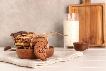 Bowl with cookies, chocolate and glass of milk on white wooden table near wall