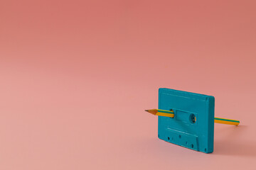 You're the pencil to my cassette tape. Old audio cassette tape and pencil on pink background. Manual rewind. Minimal vintage cassette tape concept. Retro fashion aesthetic. Retro futurism. Copy space.