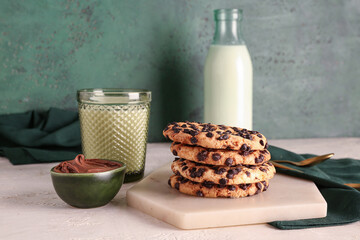 Cookies with milk, chocolate cream and spoons on white grunge table near green wall