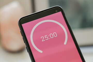 A phone with a pink and white 25-minute timer to study with the pomodoro method on a blurry...