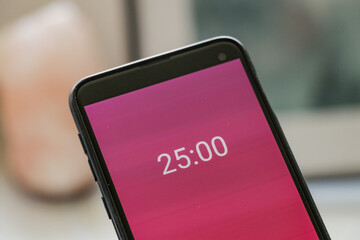 A phone with a pink and white 25-minute timer to study with the pomodoro method on a blurry background. Perfect for students planning their time studying, doing homework, being productive.