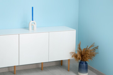 Wooden chest of drawers with candle and pampas grass near blue wall in room