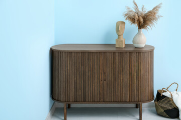 Wooden chest of drawers with pampas grass and basket near blue wall in room