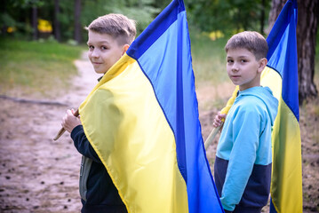Naklejka premium flags of Ukraine in hands of two boys. Children hold Ukrainian flags yellow and blue waving in wind . Ukraine's Independence Day. Flag Day