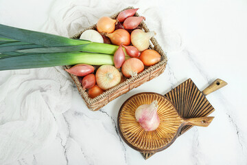 Wicker basket with different kinds of onion on light background