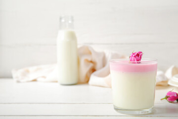 Glass of panna cotta with beautiful pink rose flowers on white wooden table