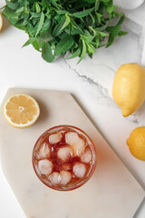 Board with glass of ice tea and lemons on white background