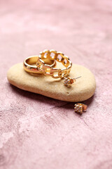 Stone with beautiful rings and earrings on pink background