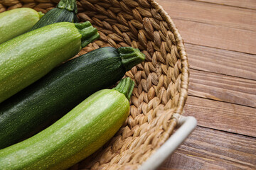 Wicker basket with fresh green zucchini on wooden background