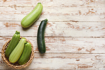 Wicker bowl with fresh green zucchini on white wooden background