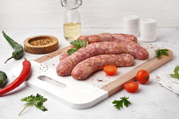 Wooden board with raw homemade sausages on light background