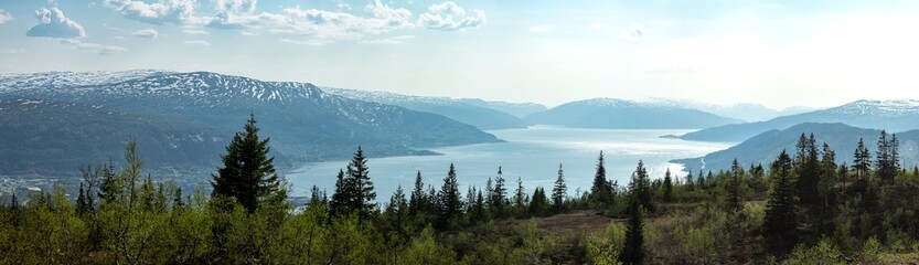 Mountain view from Risfjellet, Mo i Rana, Norway. Norwegian mountain landscape in early summer with snow on the high mountain peaks. Pine trees and high altitude. Mountain lake, fjord. Blue and green.