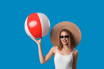 Young woman in swimsuit with beach ball on blue background