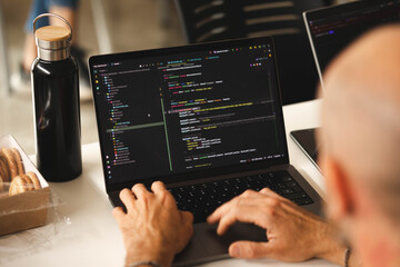 A close-up of a laptop while the hands of a man are writing code