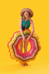 Young woman in swimsuit with inflatable ring on yellow background