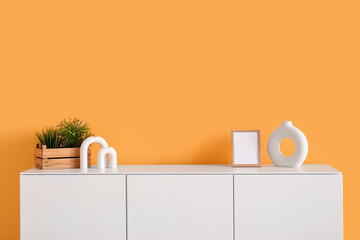 Modern chest of drawers with houseplant and decor near orange wall in room