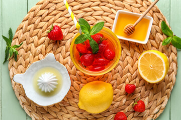 Glass of infused water with strawberry, lemon, honey and juicer on green wooden background