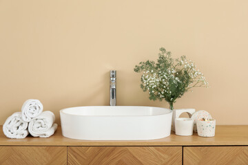 White sink, gypsophila flowers, candles and towels on chest of drawers in bathroom