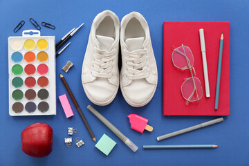 Sneakers with fresh red apple, eyeglasses and different stationery on blue background