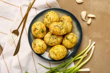 Plate of boiled baby potatoes with dill and green onion on brown background