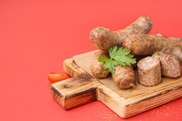 Wooden board of tasty homemade sausages on red background