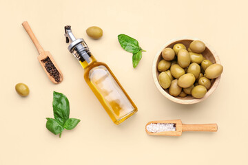 Bowl with ripe olives and bottle of oil on beige background