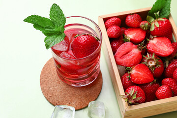 Glass of infused water and wooden box with strawberries and on green background