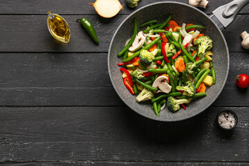 Frying pan with fresh vegetables on black wooden background