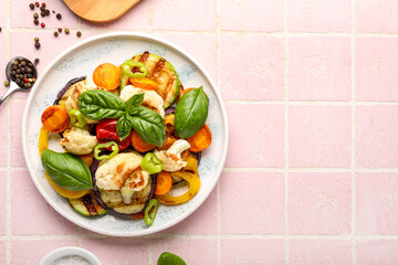 Plate with grilled vegetables and basil on pink tile background