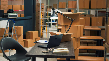 Empty desk room in storage warehouse area filled with carton boxes, office with laptop and...