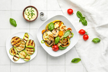 Plates with grilled vegetables and sour cream on white tile background