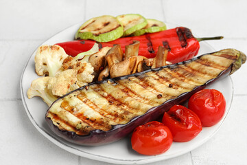 Plate with grilled vegetables and basil on white tile table