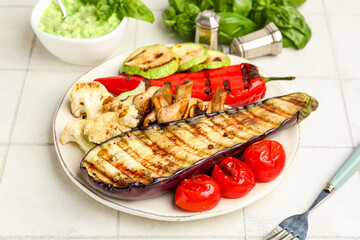 Plate with grilled vegetables and basil on white tile table