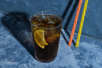 Glass of cold Cuba Libre cocktail on blue background