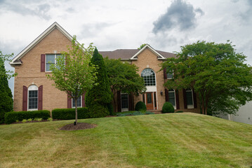 Large, beautiful, single-family brick country house. Large lawn and green trees.
