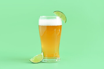 Glass of cold beer with lime on green background